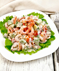 Salad with shrimp and tomato in white plate on light board