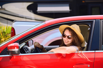 Young woman with long hair in sunglasses travels in vehicle and smiling. Beautiful girl in red car while driving. Adventures on the way to the sea. Warm summer weather. Hot sunny day