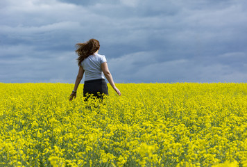 Fototapeta premium girl one, 1 runs in a field of yellow rapeseed against the blue sky