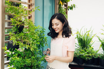 Cute asian woman gardener cutting plants with garden scissors in greenhouse