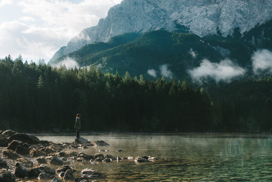 Woman gazing over a mountain lake with forest in Germany in the morning