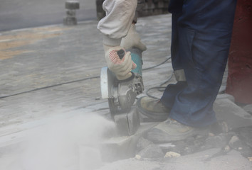 A worker mason cuts a curb with a circular saw when repair of the sidewalk