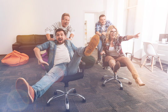 Positive Smiling Colleagues Riding In Office Chairs