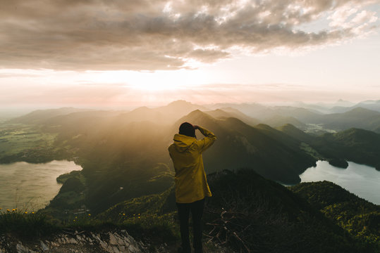 Male photographer in yellow jacket looking over a valley with mountains, forest and lake in Germany in the morning