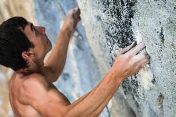 sports man climbs an overhang rock near forest and grip the hold