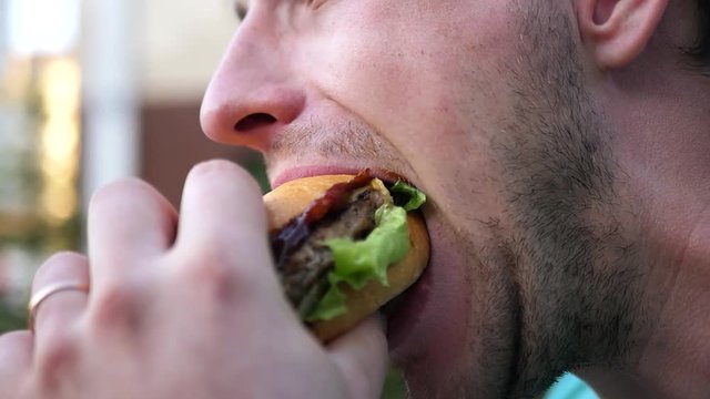 An adult man with a beard bites off a delicious juicy hamburger, smeared his face with ketchup. SLOW MOTION. HD, 1920x1080.