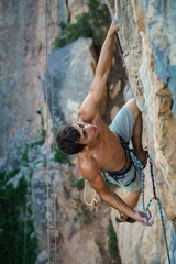 sports man climbs an overhang rock near forest and put the rope into sling