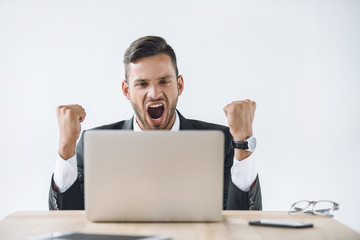 portrait of excited businessman looking at laptop screen at workplace isolated on white