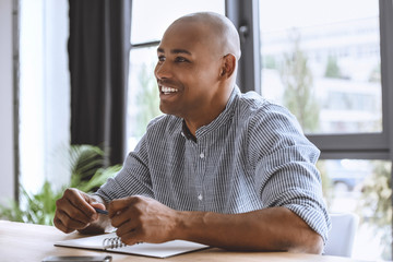 portrait of cheerful african american businessman sitting at workplace in office