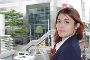 Outdoor portrait of happy young Asian business woman looking at camera in the city background.