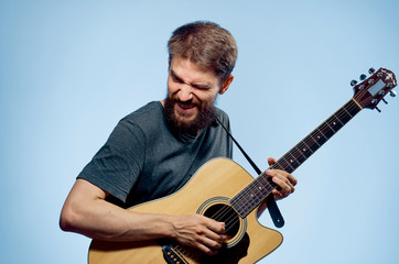Young guy with a beard on a blue background holds a guitar