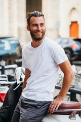 Fototapeta na wymiar Hipster handsome male model with beard wearing white blank t-shirt with space for your logo or design in casual urban style