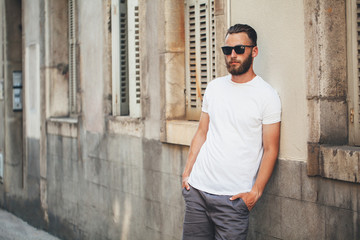 Obraz premium Hipster handsome male model with beard wearing white blank t-shirt with space for your logo or design in casual urban style