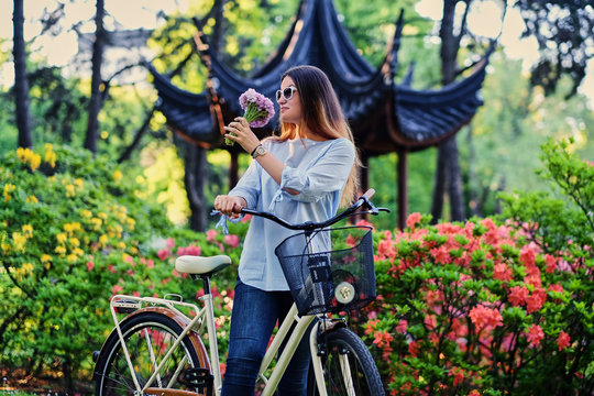 A woman with city bicycle near traditional chinese pavilion in a park.