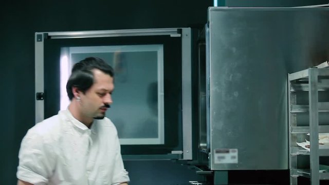 The cook put the trays with bread in the stove. The cook close the stove and fill temperature on the stove.