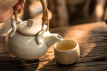 Tea pot  and cup of tea on wood table under morning light , soft focus