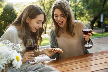 Happy young two women sitting outdoors in park drinking wine