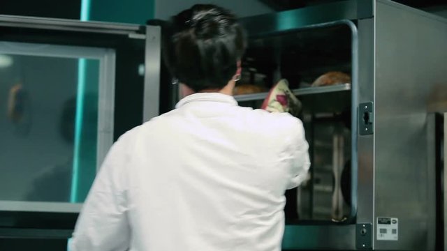 The cook take away the bread at the trays from the stove. The man put it on the table.