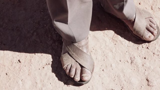 Indigenous man using artisan sandals, stepping soil of his lands.