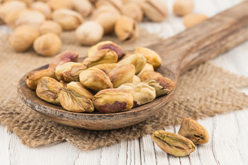 Pistachios in a wooden spoon on the old white wooden table.