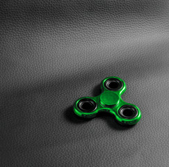 Green  fidget spinner toy. backdrop is Genuine black leather ,focus on device. Close up , photo...