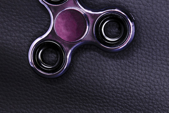Pink shining  fidget spinner toy. backdrop is Genuine black leather ,focus on device. Close up , photo from above ,top.