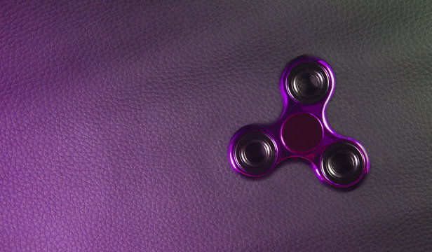 Pink shining  fidget spinner toy. backdrop is Genuine black leather ,focus on device. Close up , photo from above ,top.
