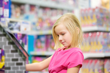 Adorable girl in pink explore toys in kids supermarket