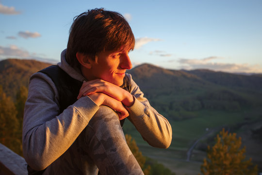A young man, at the top of the mountain, watches the sun go down.