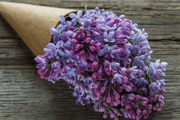 Lilac flowers bouquet in a craft paper cornet on the old wooden background