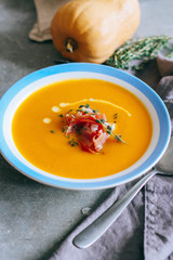 A plate of pumpkin soup, with prosciutto and thyme, on a gray background