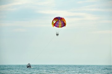 Beach vacation at sea. Holidaymakers tourists fly high in sky on multi-colored parachute, which pulls boat on its rope