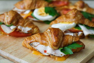Mini croissant sandwiches with chicken ham, melted cheese and green parsley served with other hot sandwiches on wooden table