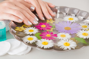 Obraz na płótnie Canvas Woman washing her hands in the bowl of water. Cares about a clean and soft hands skin. Fresh and fragrant daisy flowers in the water.