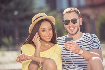 young happy multiethnic couple smiling and listening music with earphones on smartphone
