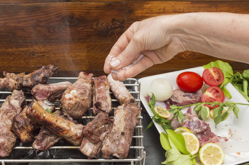 Roasted pork ribs on the barbecue, a hand puts the salt in the meat