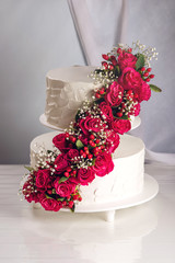 A large tiered wedding cake decorated with red roses on the table