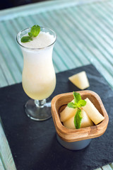Fresh white smoothie in a glass with sliced pieces of melon and mint on a blue wooden background. Summer cool drinks