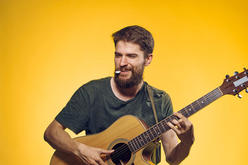 Young guy with a beard on a yellow background holds a guitar