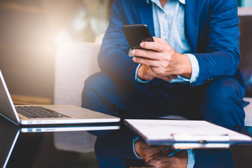 Handsome businessman in suit and eyeglasses speaking on the phone in office,Side view shot of a man's hands using smart phone in rear view of business man busy using cell phone at office.