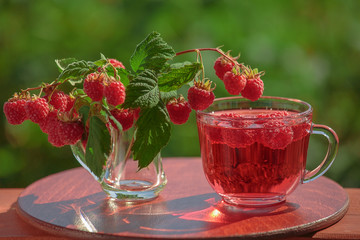A colorful picture of raspberries and soda water in glass with a natural green background. Natural backlighting. The concept of summer, heat, recreation.