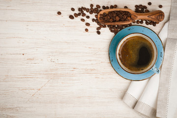 Coffee cup, spoon with beans and tablecloth on wooden table