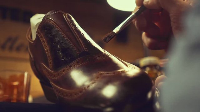 Close up of a shoemaker hands smearing special liquid paint with a brush on a shoe at the workshop