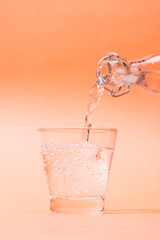 Pouring water from bottle to glass on orange background