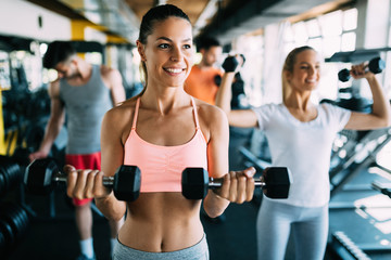 Fototapeta na wymiar Young attractive woman with friends doing exercises in gym