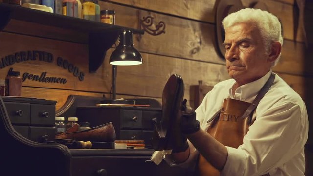 Senior bootmaker holding and polishing a leather shoe while sitting at the workshop