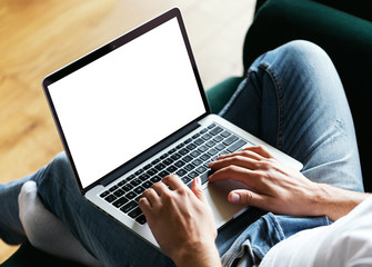Man's hands using laptop with blank screen on desk in home interior. Work concept