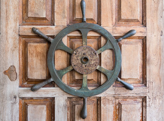 Old boat steering wheel on wooden door.