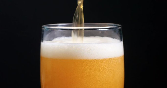 Pouring lager beer on a pint glass with black background