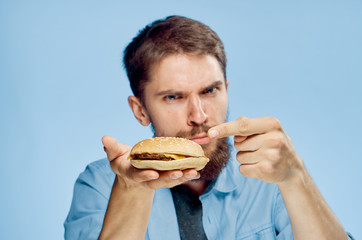 Young guy with a beard on a blue background holds a hamburger